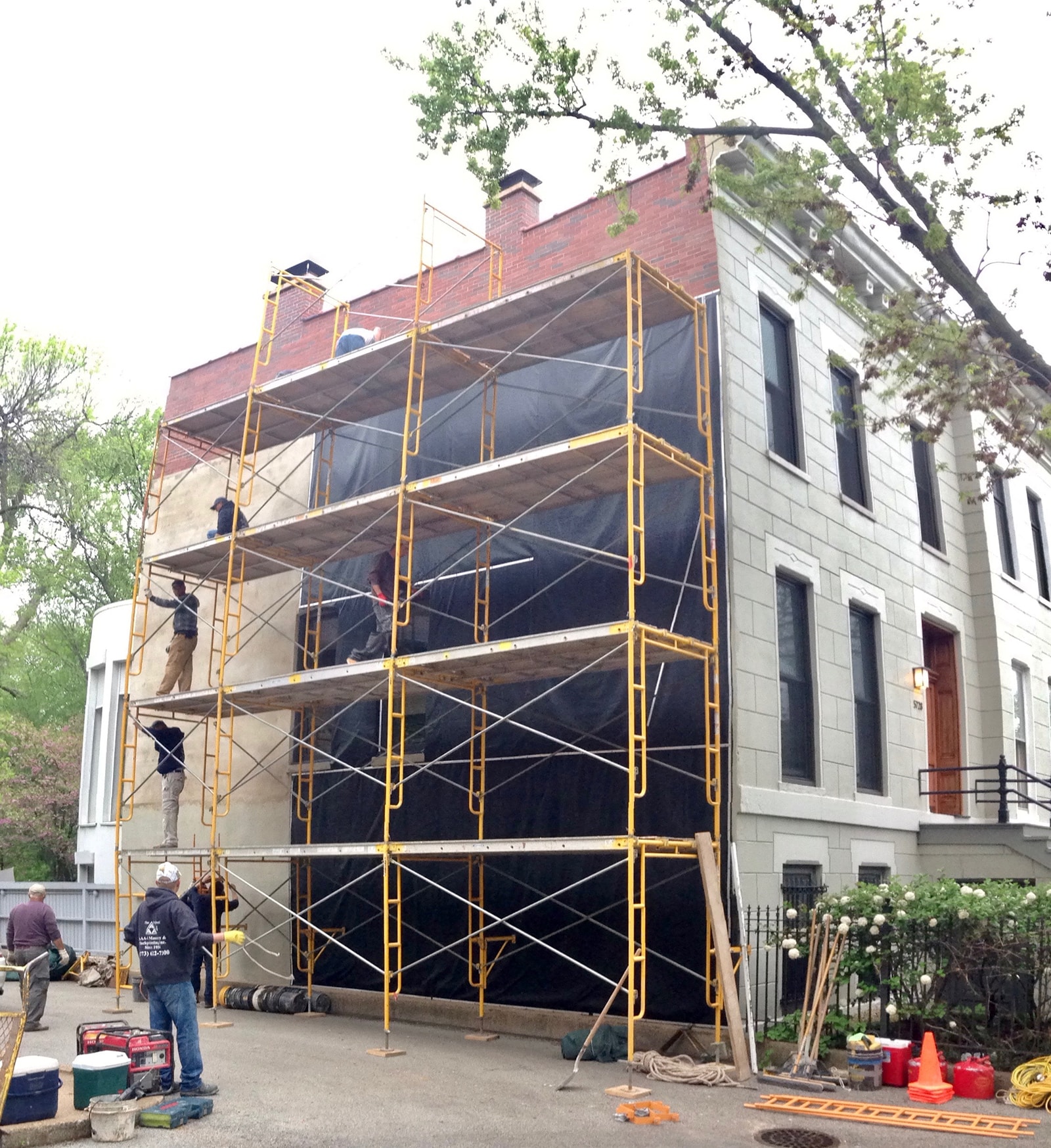 Workers installing vinyl tarpaulins on wall of masonry building