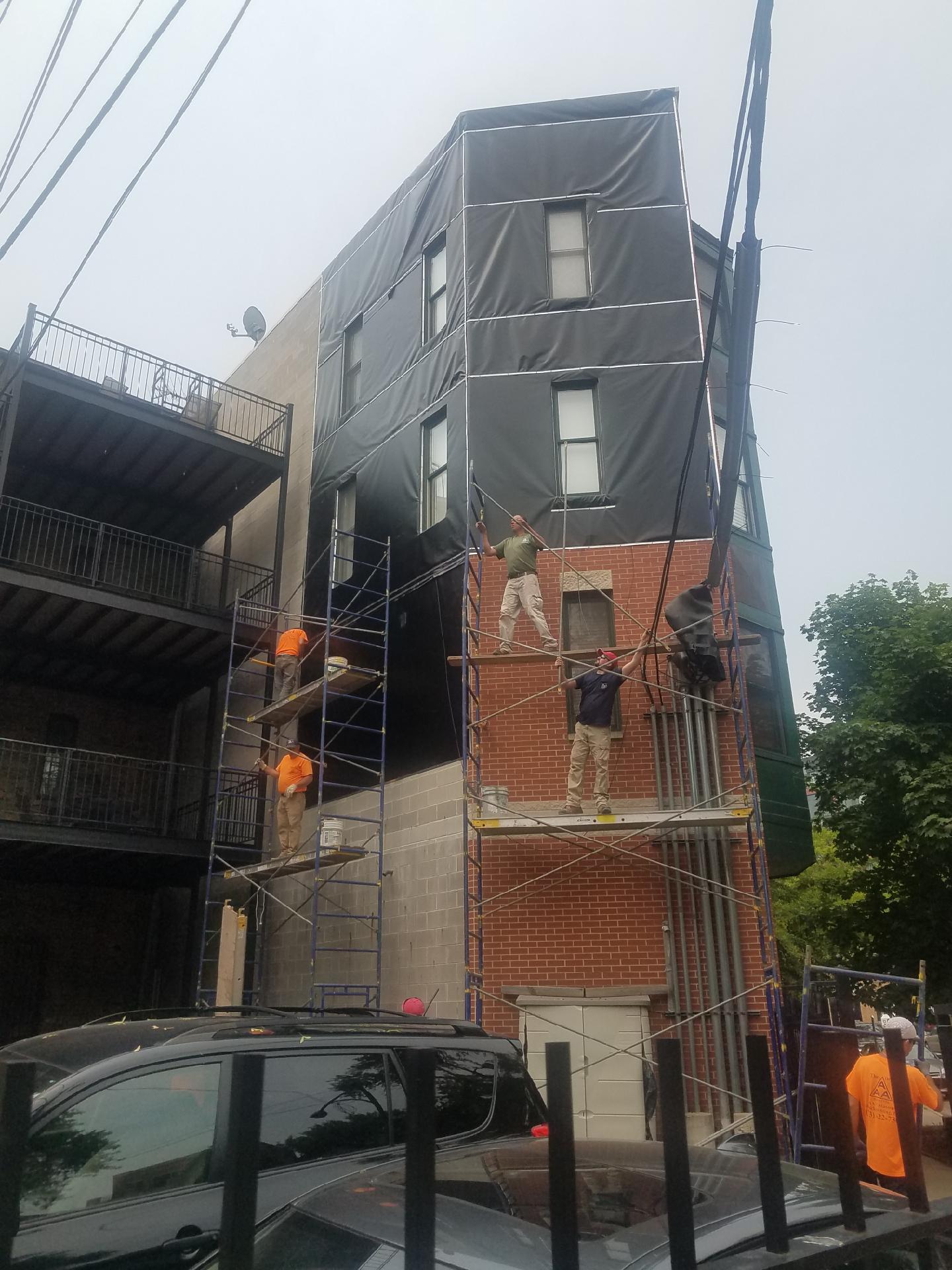 Workers installing heavy-duty vinyl tarpaulins on a building in Lincoln Park, Chicago