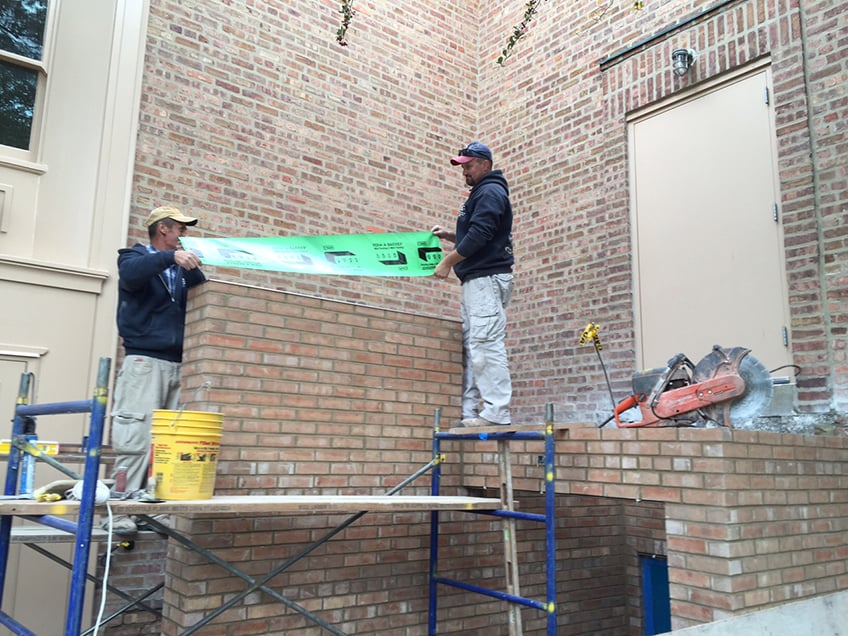 Two masons placing drip edges and flashing on new wall of staircase up.