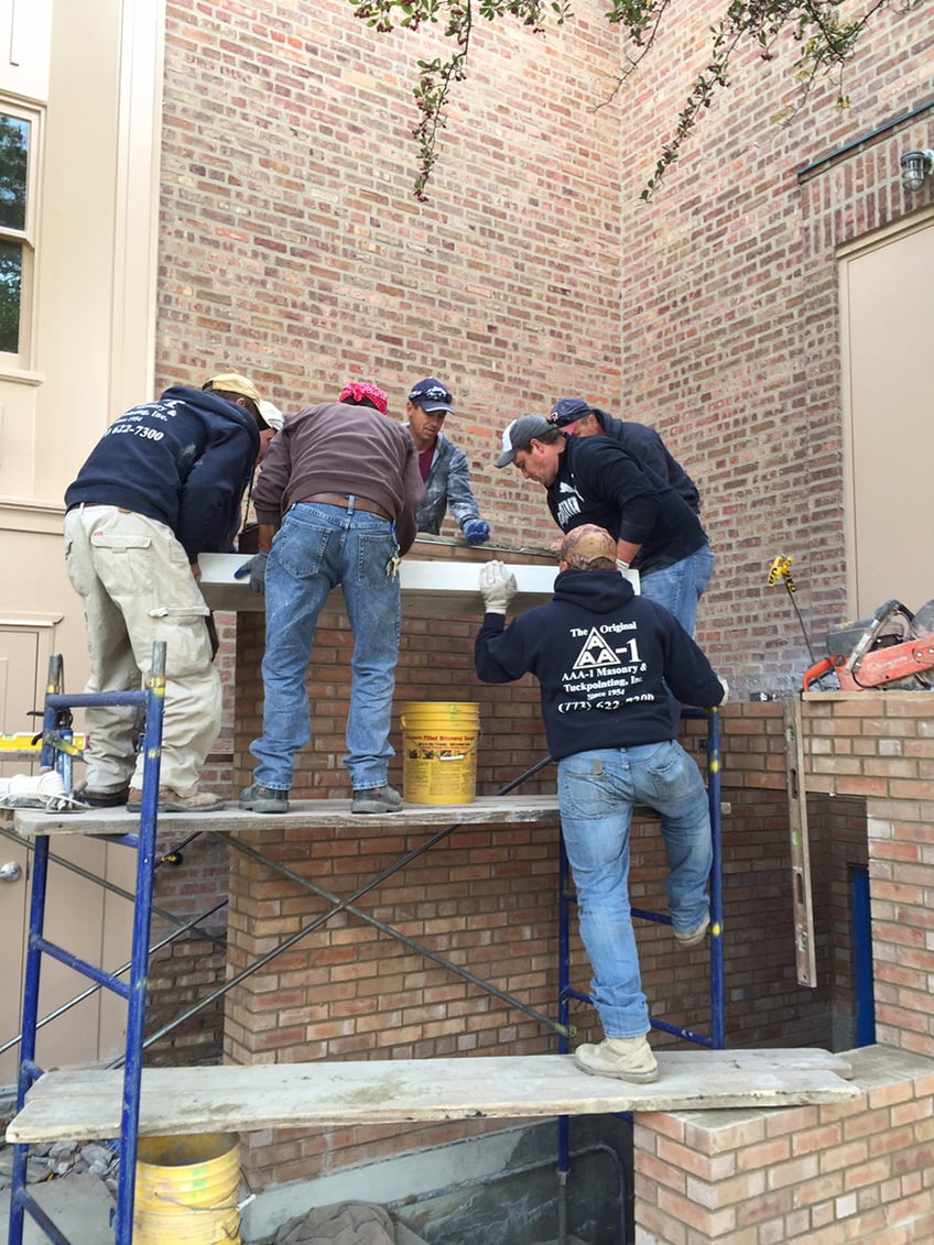 Limestone capstone being placed on new wall by seven masons.