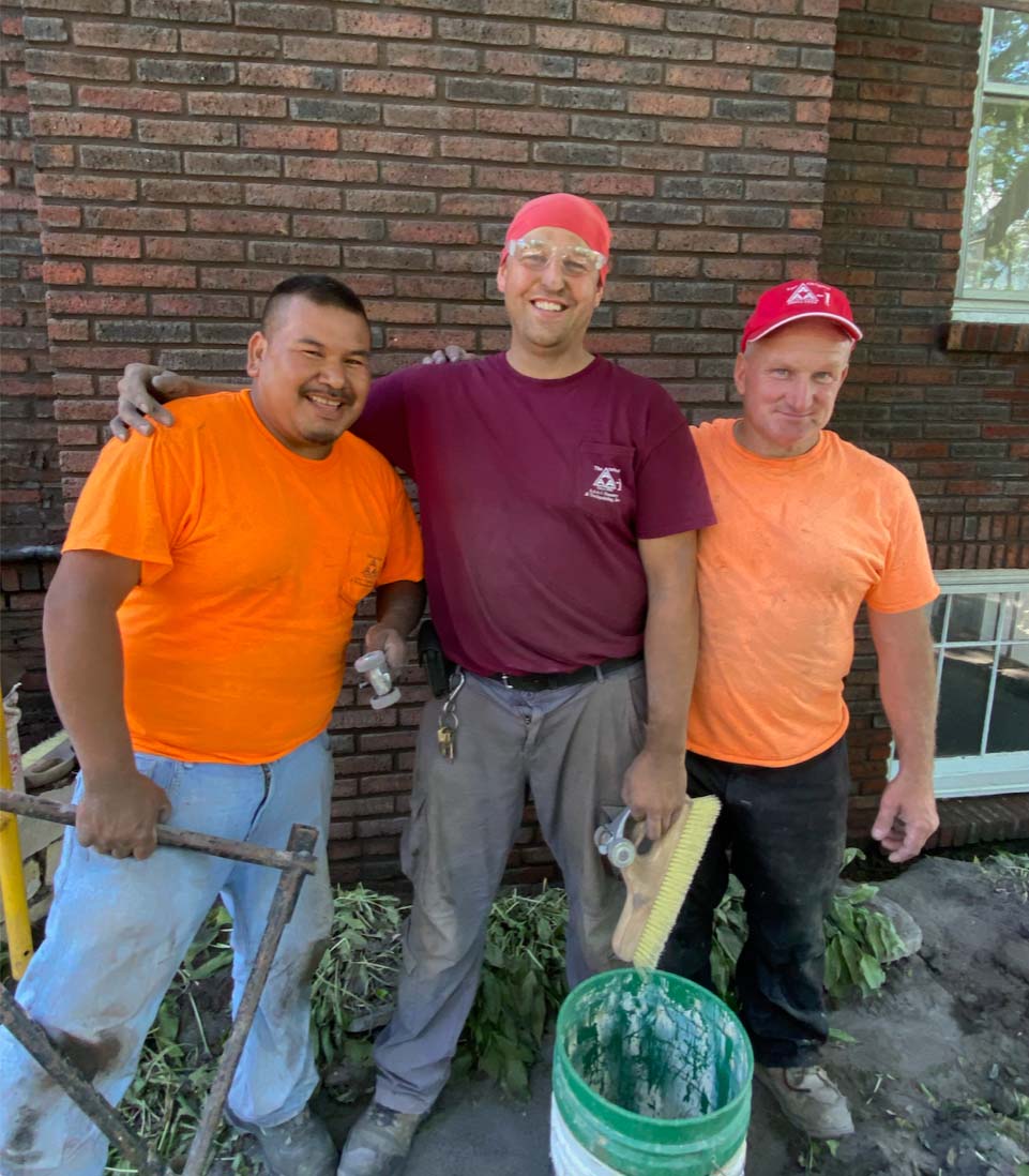 Greg, Jack, and Jesus standing in front of brick home