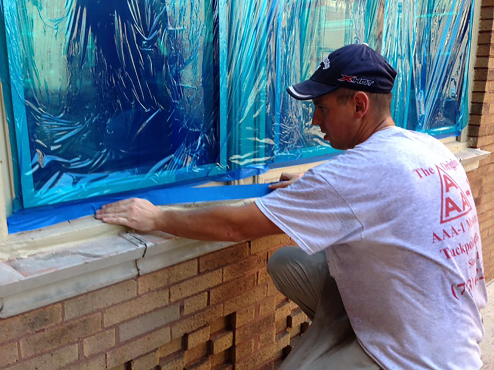 An AAA-1 licensed mason contractor protecting 100-year-old windows and window frames with plastic window film and blue tape.