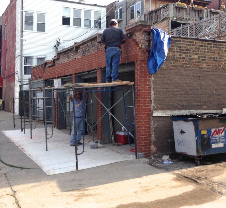 Masons dangerously and improperly restoring a garage parapet wall.