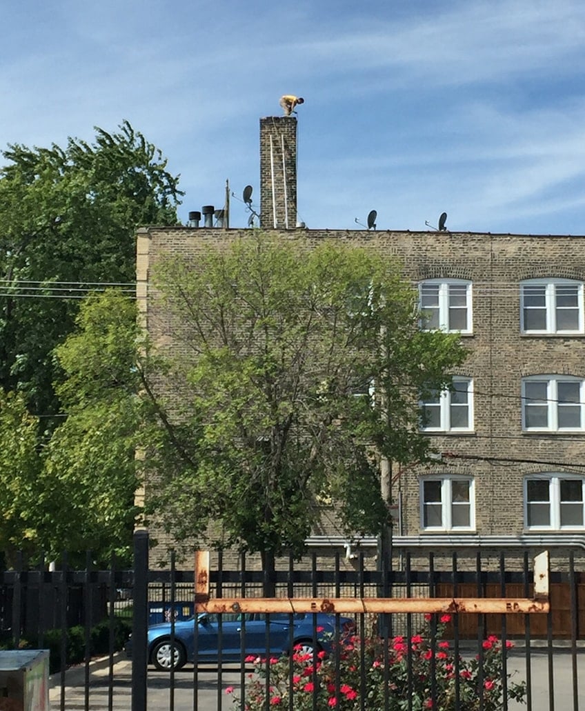 A mason working in dangerous conditions on top of a chimney