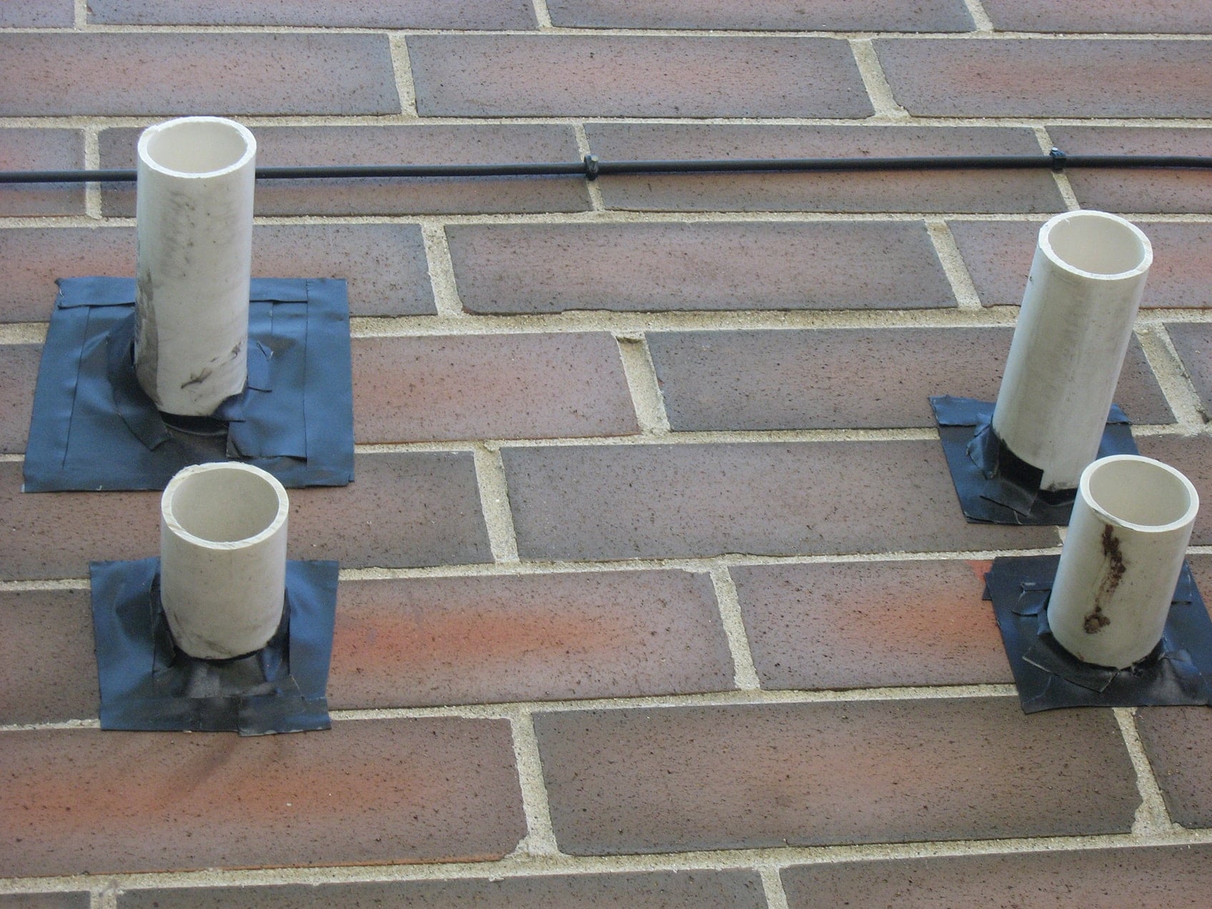 Surface-applied adhesive flashing around four PVC exhaust tubes on a masonry wall